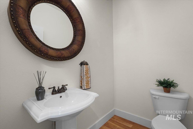 bathroom featuring baseboards, a sink, wood finished floors, and toilet