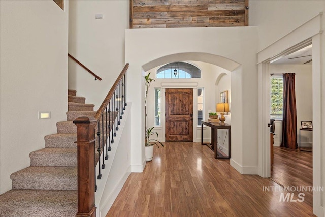 entrance foyer featuring stairs, wood finished floors, baseboards, a high ceiling, and arched walkways