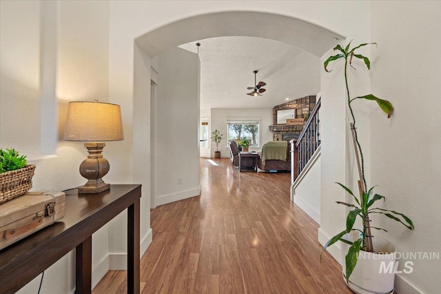 hallway featuring arched walkways, baseboards, and wood finished floors