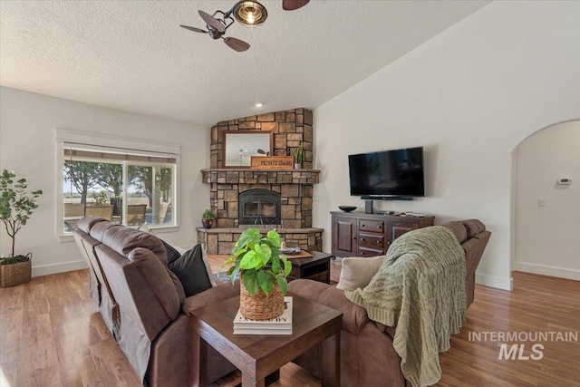living area featuring wood finished floors, lofted ceiling, ceiling fan, a textured ceiling, and arched walkways