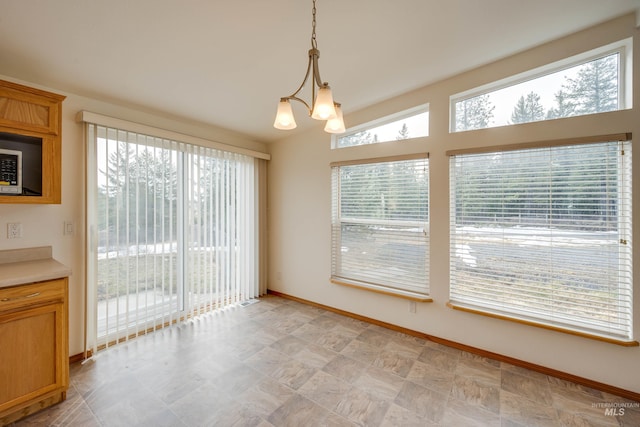 unfurnished dining area with a notable chandelier, a healthy amount of sunlight, and baseboards