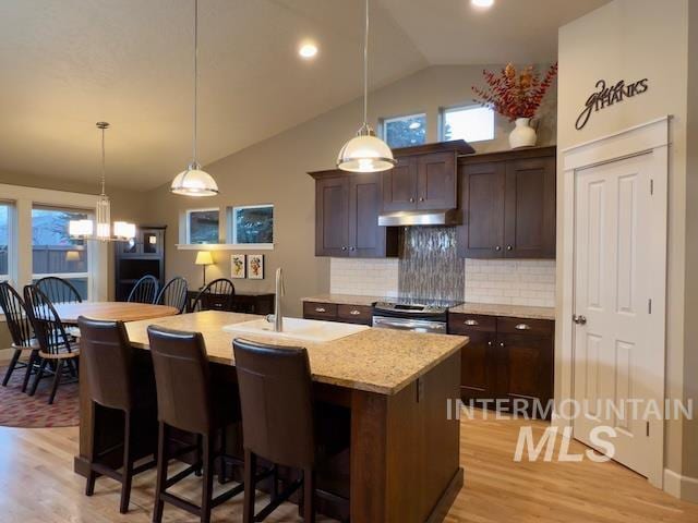 kitchen with stainless steel electric stove, a kitchen bar, a center island with sink, and dark brown cabinetry