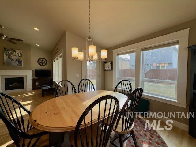 dining area with lofted ceiling, ceiling fan with notable chandelier, and light hardwood / wood-style flooring