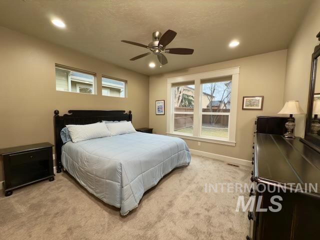 bedroom featuring ceiling fan, light colored carpet, multiple windows, and a textured ceiling