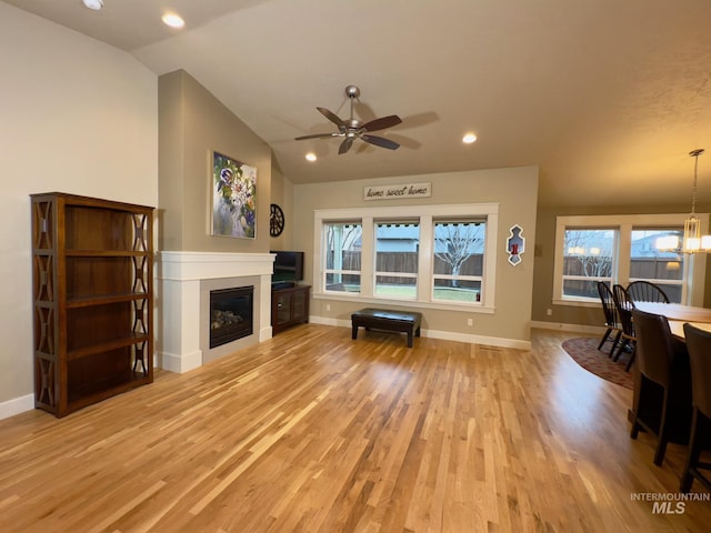 living room with vaulted ceiling, ceiling fan with notable chandelier, and light hardwood / wood-style floors