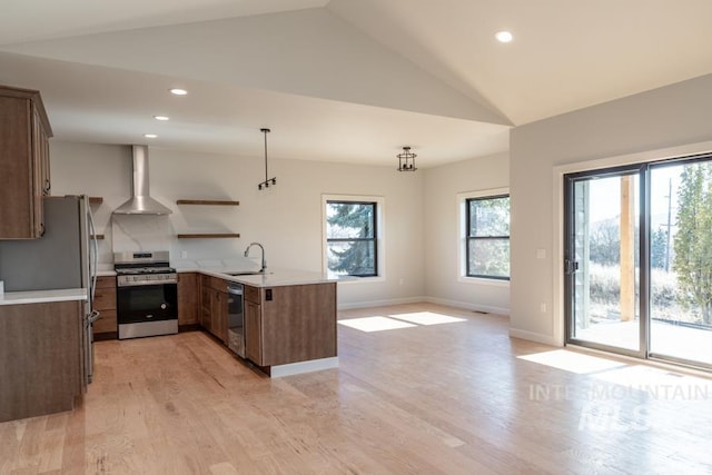 kitchen featuring stainless steel appliances, a peninsula, a sink, wall chimney range hood, and open shelves