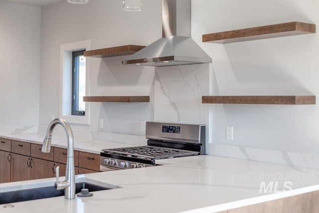 kitchen with stainless steel gas range, open shelves, a sink, and exhaust hood