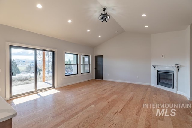 unfurnished living room with vaulted ceiling, light wood finished floors, a glass covered fireplace, and baseboards