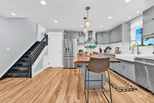 kitchen with stainless steel appliances, gray cabinets, wall chimney exhaust hood, a sink, and recessed lighting