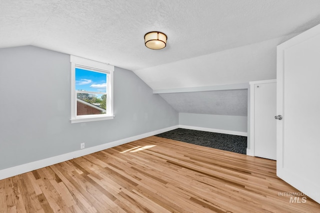 additional living space featuring wood finished floors, baseboards, lofted ceiling, and a textured ceiling