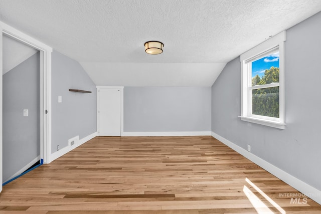 bonus room featuring lofted ceiling, a textured ceiling, light wood-type flooring, and baseboards