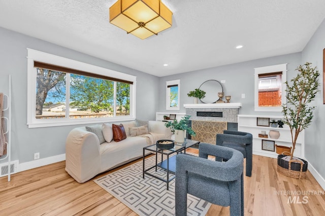 living area with wood finished floors, baseboards, a fireplace, a textured ceiling, and recessed lighting
