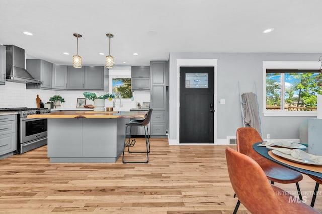 kitchen featuring wall chimney exhaust hood, gas stove, gray cabinetry, butcher block countertops, and recessed lighting