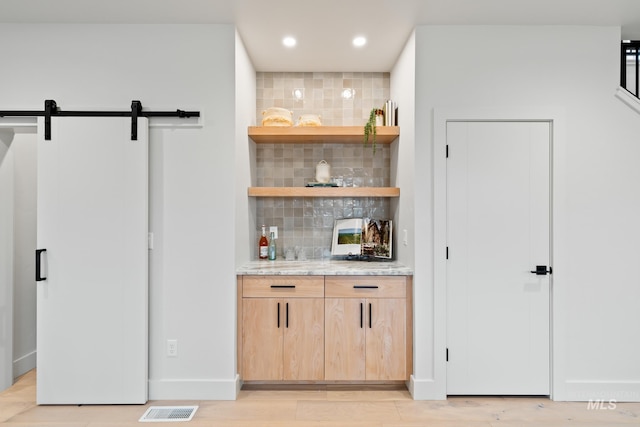 bar with light hardwood / wood-style flooring, backsplash, a barn door, and light brown cabinets