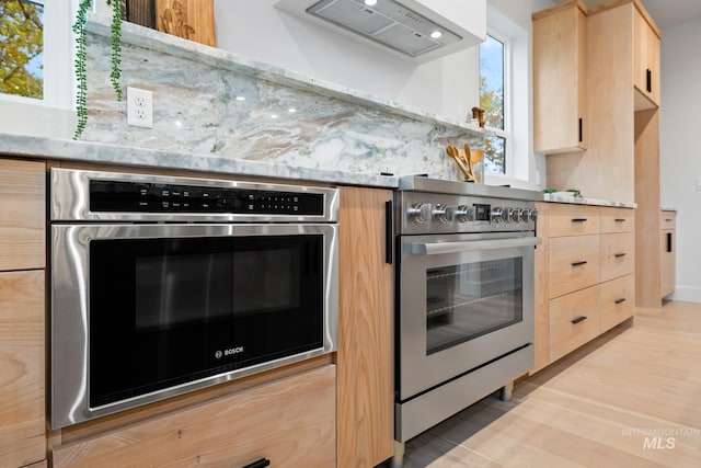 kitchen with custom exhaust hood, light hardwood / wood-style floors, backsplash, appliances with stainless steel finishes, and light brown cabinets