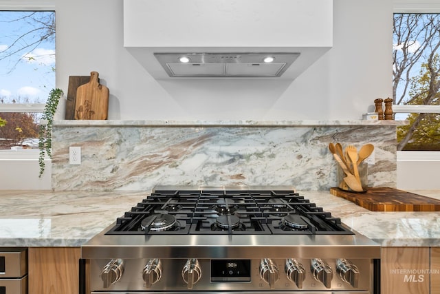 room details with tasteful backsplash, island exhaust hood, light stone counters, and gas range