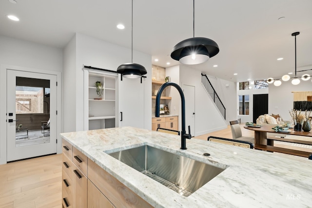 kitchen featuring sink, light stone counters, light brown cabinets, light hardwood / wood-style flooring, and hanging light fixtures