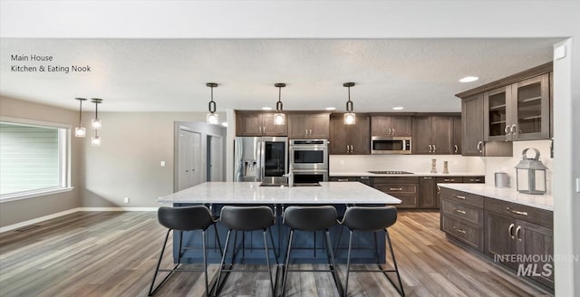 kitchen with appliances with stainless steel finishes, wood finished floors, baseboards, dark brown cabinetry, and recessed lighting