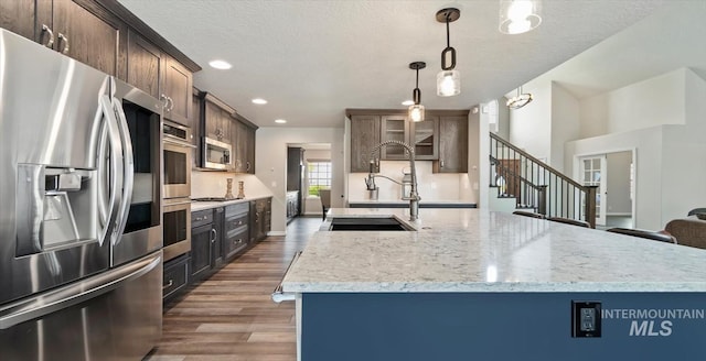 kitchen with stainless steel appliances, wood finished floors, a sink, decorative light fixtures, and light stone countertops