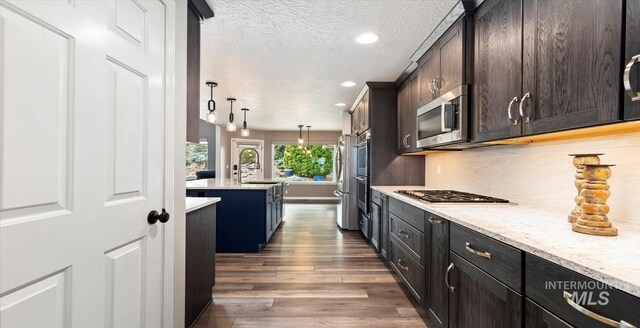 kitchen featuring appliances with stainless steel finishes, dark wood-style flooring, a textured ceiling, recessed lighting, and a kitchen island with sink