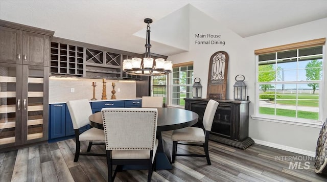 dining area with a chandelier, dark wood-style flooring, baseboards, and lofted ceiling