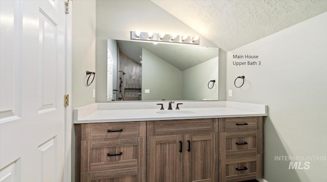 bathroom with vaulted ceiling, a textured ceiling, and vanity