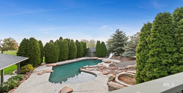 outdoor pool with a water slide, a shed, and an outdoor structure