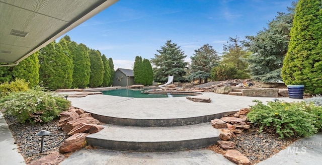 swimming pool featuring a water slide, a shed, a patio area, and an outdoor structure