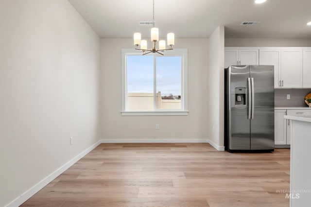 kitchen featuring stainless steel fridge with ice dispenser, a notable chandelier, pendant lighting, decorative backsplash, and white cabinets