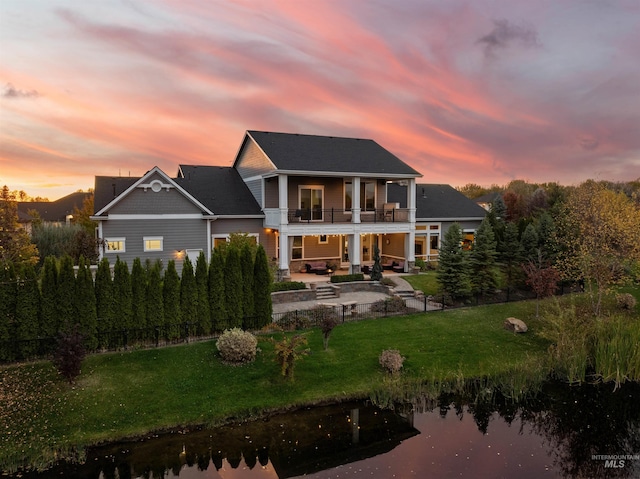 back house at dusk with a yard, a water view, a balcony, and a patio