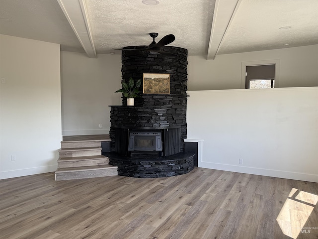 unfurnished living room featuring baseboards, a stone fireplace, beam ceiling, and wood finished floors
