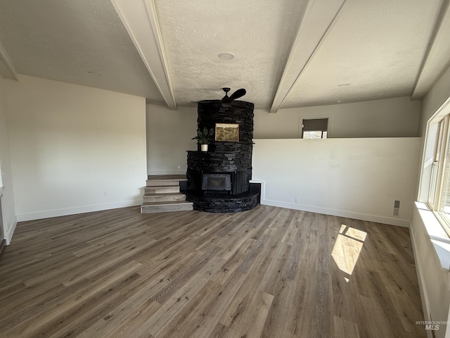 unfurnished living room with wood finished floors, a healthy amount of sunlight, beamed ceiling, baseboards, and a textured ceiling
