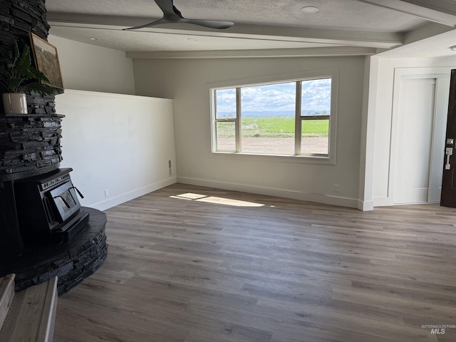 unfurnished living room featuring a wood stove, a textured ceiling, ceiling fan, and wood finished floors
