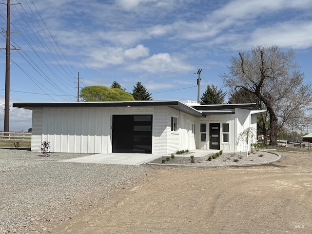 view of front of home featuring board and batten siding, brick siding, an attached garage, and dirt driveway