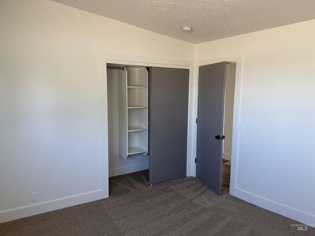 unfurnished bedroom with baseboards, a closet, dark carpet, and a textured ceiling