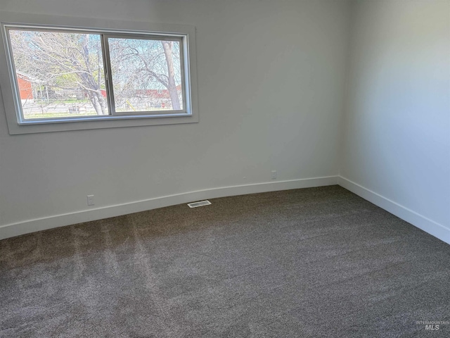 empty room featuring dark carpet, baseboards, visible vents, and a wealth of natural light