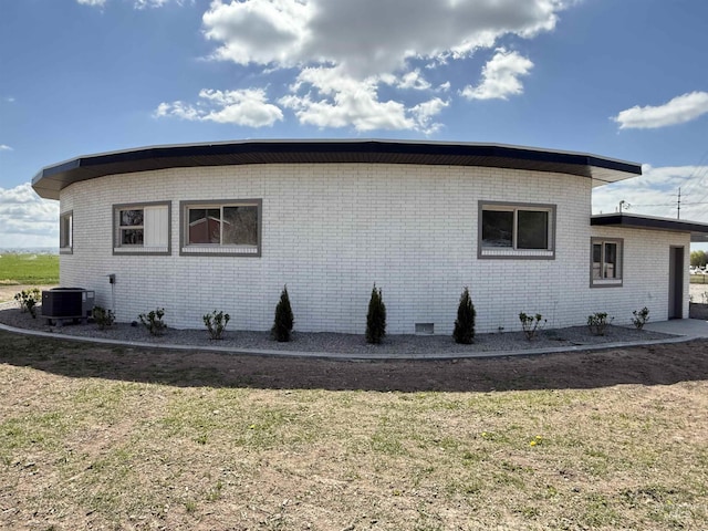 view of property exterior featuring a lawn, central AC unit, and brick siding