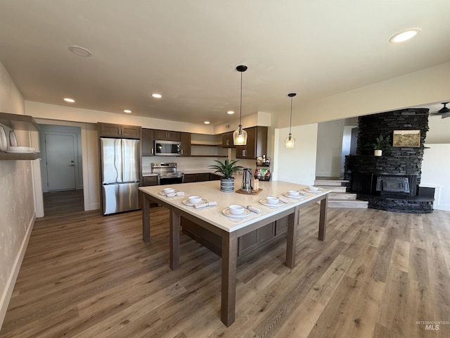 kitchen with dark brown cabinets, appliances with stainless steel finishes, light wood-style flooring, decorative light fixtures, and baseboards