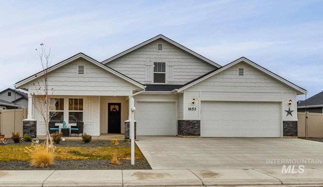 view of front of house with concrete driveway, a porch, stone siding, and fence