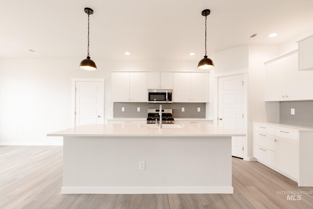 kitchen featuring sink, white cabinetry, hanging light fixtures, stainless steel appliances, and a center island with sink