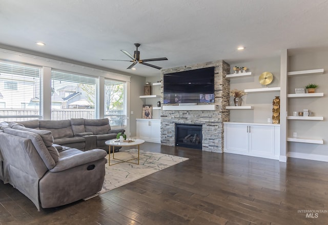 living area featuring ceiling fan, a stone fireplace, and wood-type flooring