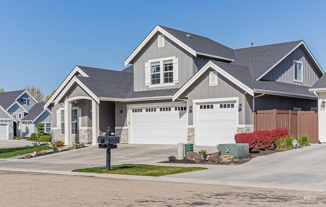 craftsman-style home featuring board and batten siding, concrete driveway, stone siding, fence, and a garage