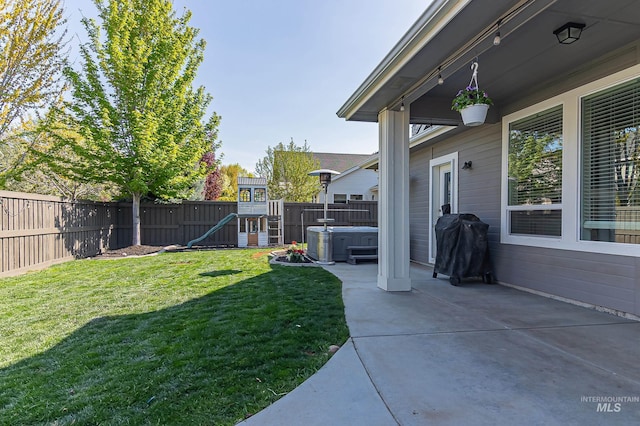 view of yard with a fenced backyard, a hot tub, a playground, and a patio area