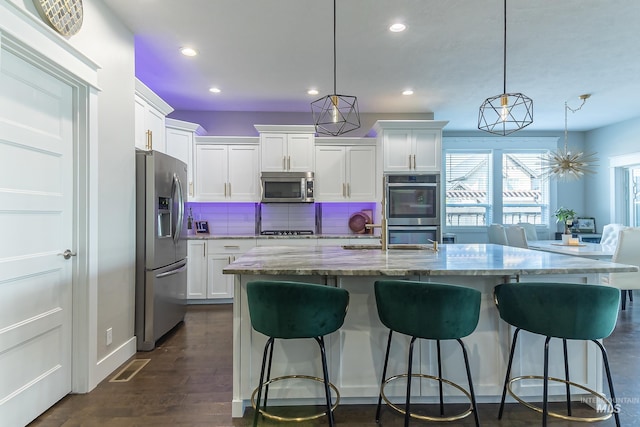 kitchen featuring recessed lighting, stainless steel appliances, a kitchen breakfast bar, light stone counters, and white cabinetry