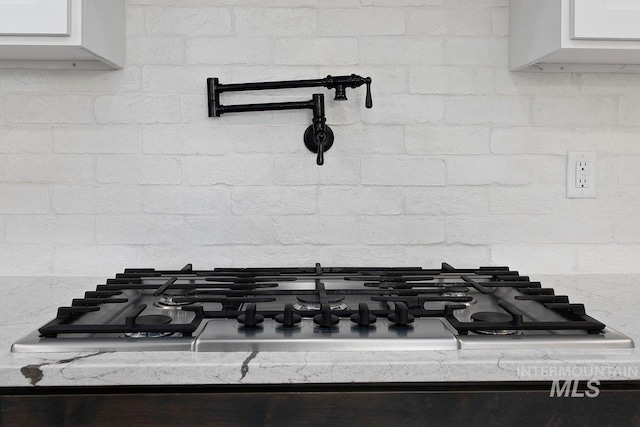 details featuring white cabinets, tasteful backsplash, and stainless steel gas cooktop