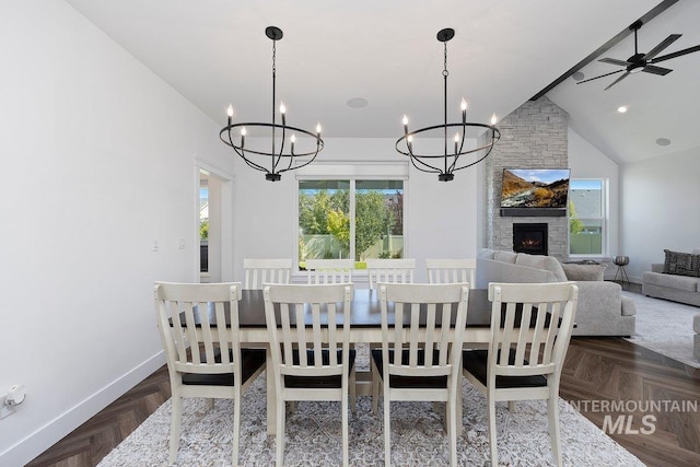 dining room featuring high vaulted ceiling, a stone fireplace, ceiling fan with notable chandelier, and baseboards