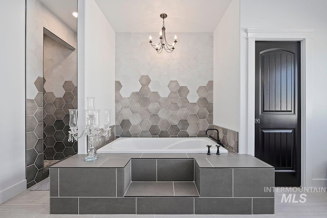 full bathroom with tile patterned flooring, a notable chandelier, tile walls, and a garden tub