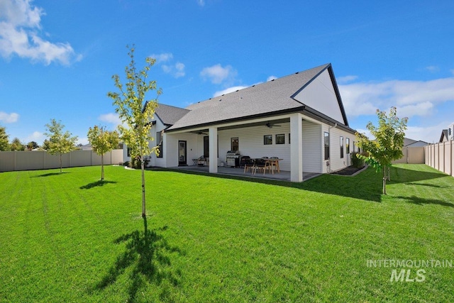 rear view of property featuring a ceiling fan, a fenced backyard, a shingled roof, a patio, and a lawn