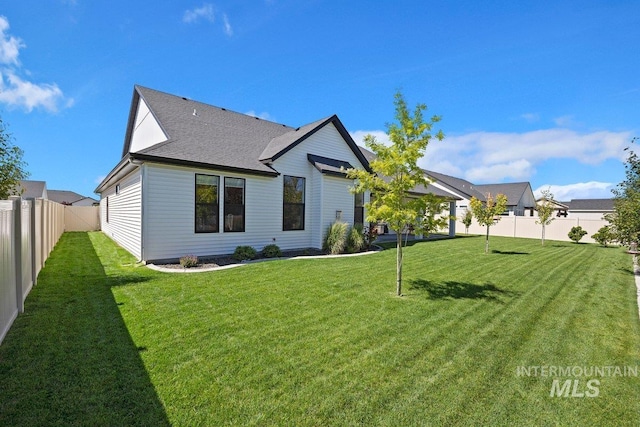 back of property with a fenced backyard, roof with shingles, and a yard