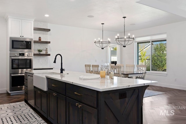 kitchen featuring a kitchen island with sink, stainless steel appliances, white cabinetry, a sink, and open shelves